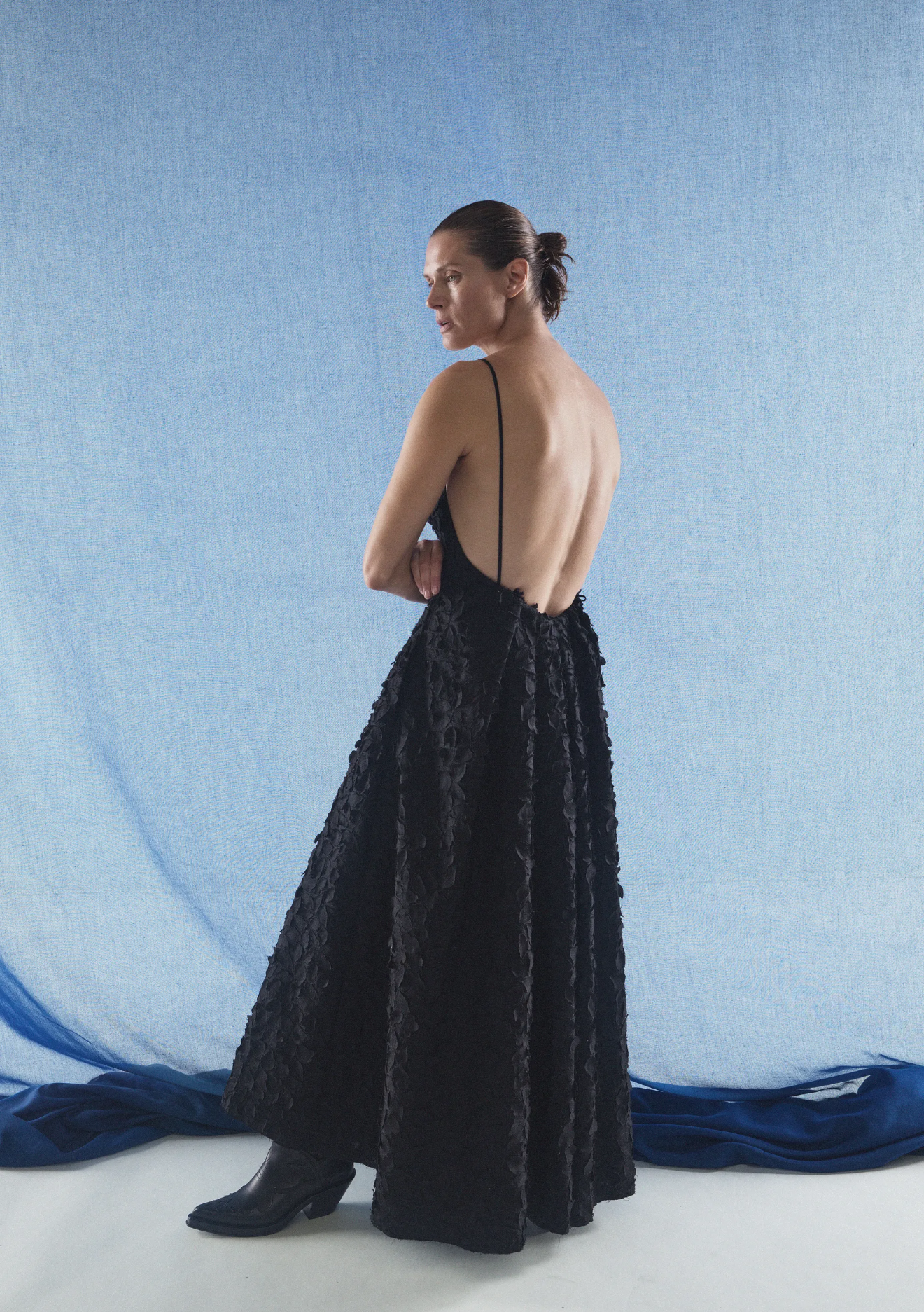 Woman in a black evening gown with a blue draped fabric in the background