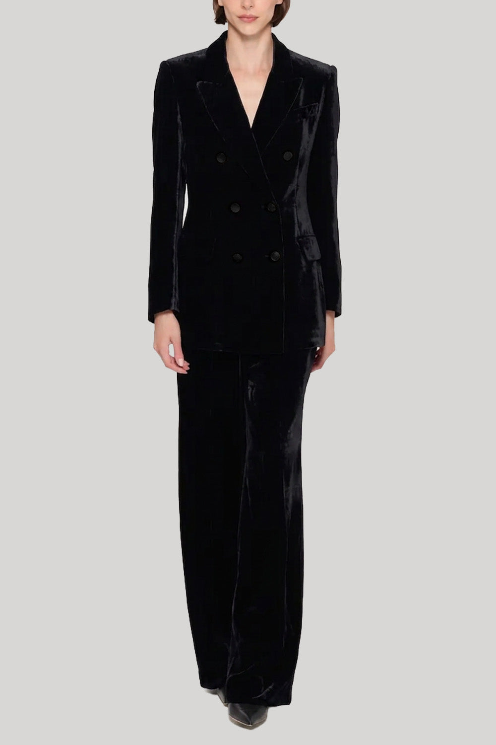 A model wearing a black velvet double-breasted blazer and matching wide-leg trousers from Parosh against a solid light gray background.