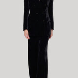 A model wearing a black velvet double-breasted blazer and matching wide-leg trousers from Parosh against a solid light gray background.