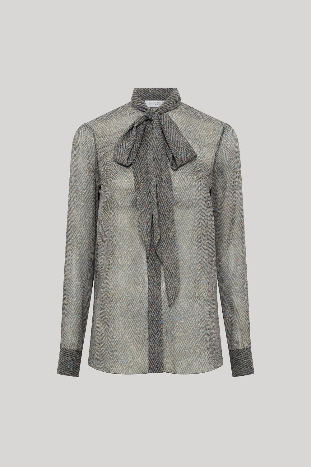 A gray and black herringbone patterned long-sleeve blouse with a large bow tie at the collar, from Gabriela Hearst, shown on a neutral light gray background.