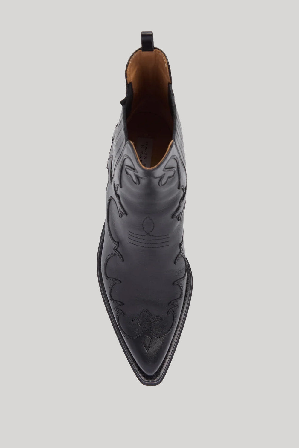 A top-down view of a black leather pointed-toe western boot with decorative stitching and a pull tab, shown on a light gray background.