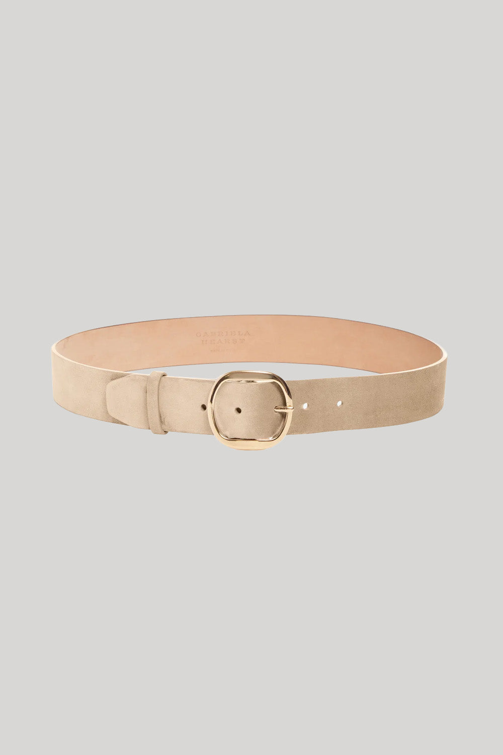 A light beige leather belt with a gold-tone buckle, from Gabriela Hearst, displayed in a curved shape on a solid light gray background.