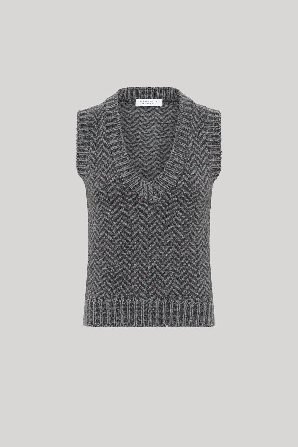 A sleeveless knit sweater vest with a V-neck and a gray and black herringbone pattern, from Gabriela Hearst, shown against a solid light gray background.