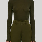 A model wearing a ribbed olive green mock neck long-sleeve top and matching olive green trousers, from Gabriela Hearst, shown from the mouth down against a solid light gray background.