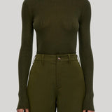 A model wearing a ribbed olive green mock neck long-sleeve top and matching olive green trousers, from Gabriela Hearst, shown from the mouth down against a solid light gray background.