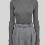 A model wearing a ribbed gray long-sleeve turtleneck sweater paired with high-waisted gray pleated trousers and a matching belt, from Gabriela Hearst, shown against a solid light gray background.