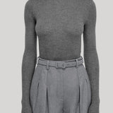 A model wearing a ribbed gray long-sleeve turtleneck sweater paired with high-waisted gray pleated trousers and a matching belt, from Gabriela Hearst, shown against a solid light gray background.
