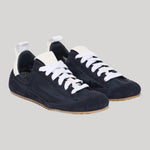A pair of low-top sneakers in dark navy blue suede with white laces, white pull tabs, and light brown gum soles, shown on a solid light gray background.