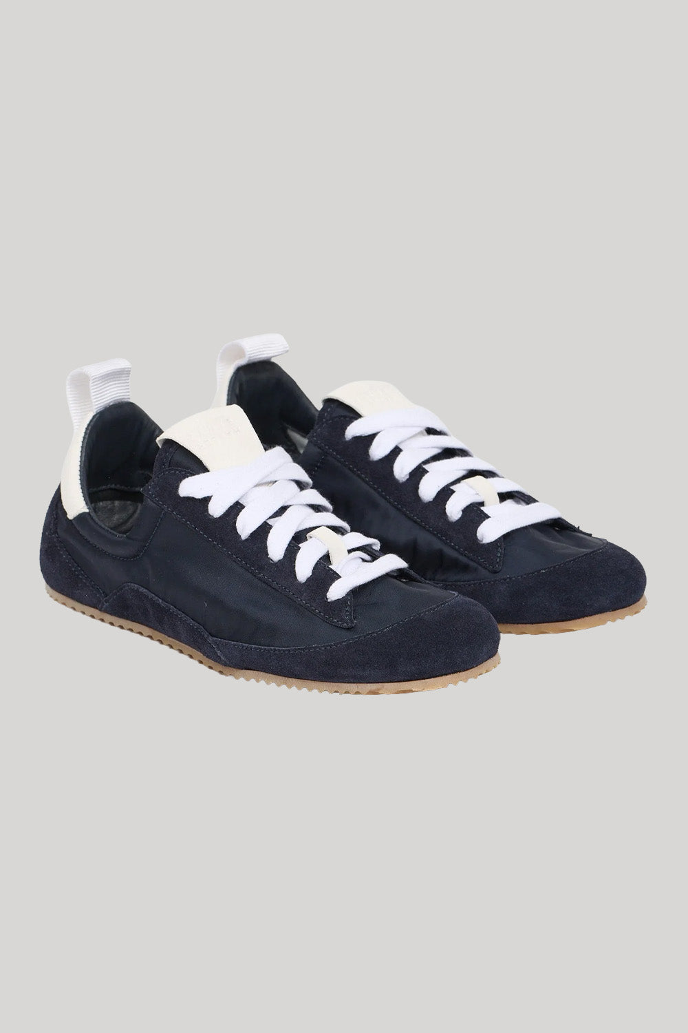 A pair of low-top sneakers in dark navy blue suede with white laces, white pull tabs, and light brown gum soles, shown on a solid light gray background.