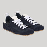 A pair of low-top sneakers in dark navy blue suede with white laces, white pull tabs, and light brown gum soles, shown on a solid light gray background.