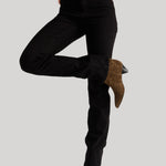 A model wearing black high-rise jeans, styled with a gray t-shirt and brown suede ankle boots, captured from the waist down against a solid light gray background.
