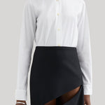 A model wearing a white long-sleeve Jil Sander button-up shirt tucked into a black asymmetrical wrap skirt with a diagonal slit, photographed against a neutral light gray background.