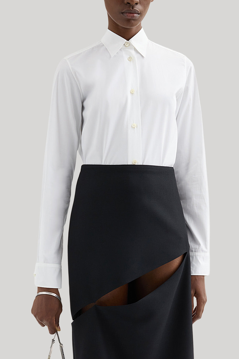 A model wearing a white long-sleeve Jil Sander button-up shirt tucked into a black asymmetrical wrap skirt with a diagonal slit, photographed against a neutral light gray background.