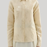 Front view of a woman wearing a cream-colored long-sleeve blouse with a subtle tonal floral jacquard pattern, paired with a matching cream skirt, against a solid light gray background. The shirt is Jil Sander 