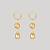 A pair of gold drop hoop earrings with a circular bead and teardrop pendant, shown against a solid light gray background.