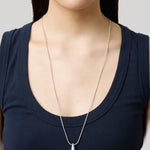 A silver teardrop pendant necklace worn by a model in a navy blue tank top against a light gray background.