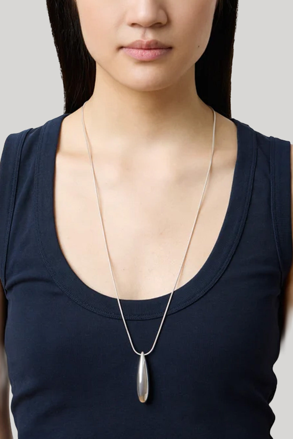 A silver teardrop pendant necklace worn by a model in a navy blue tank top against a light gray background.