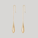 A pair of gold teardrop-shaped dangle earrings with curved hook backs, displayed against a solid light gray background.