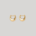 A pair of gold crescent-shaped hoop earrings on a solid light gray background.