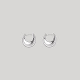 A pair of polished silver crescent-shaped hoop earrings on a solid light gray background.