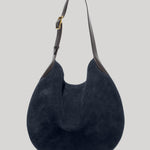 A dark navy blue suede hobo shoulder bag  from Nili Lotan with dark brown leather trim and a gold-tone buckle on the strap , shown against a solid light gray background.