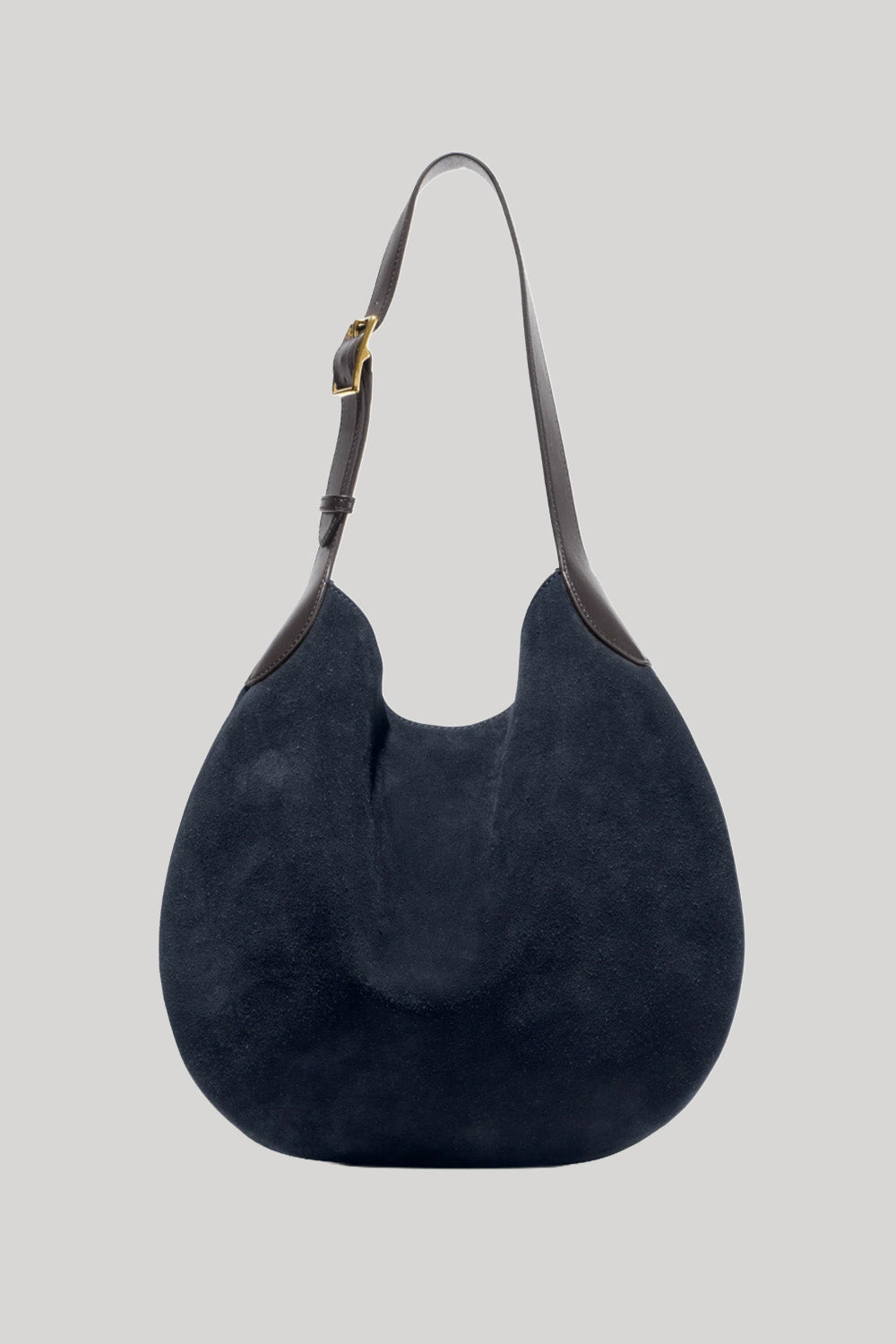 A dark navy blue suede hobo shoulder bag  from Nili Lotan with dark brown leather trim and a gold-tone buckle on the strap , shown against a solid light gray background.