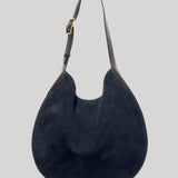 A dark navy blue suede hobo shoulder bag  from Nili Lotan with dark brown leather trim and a gold-tone buckle on the strap , shown against a solid light gray background.