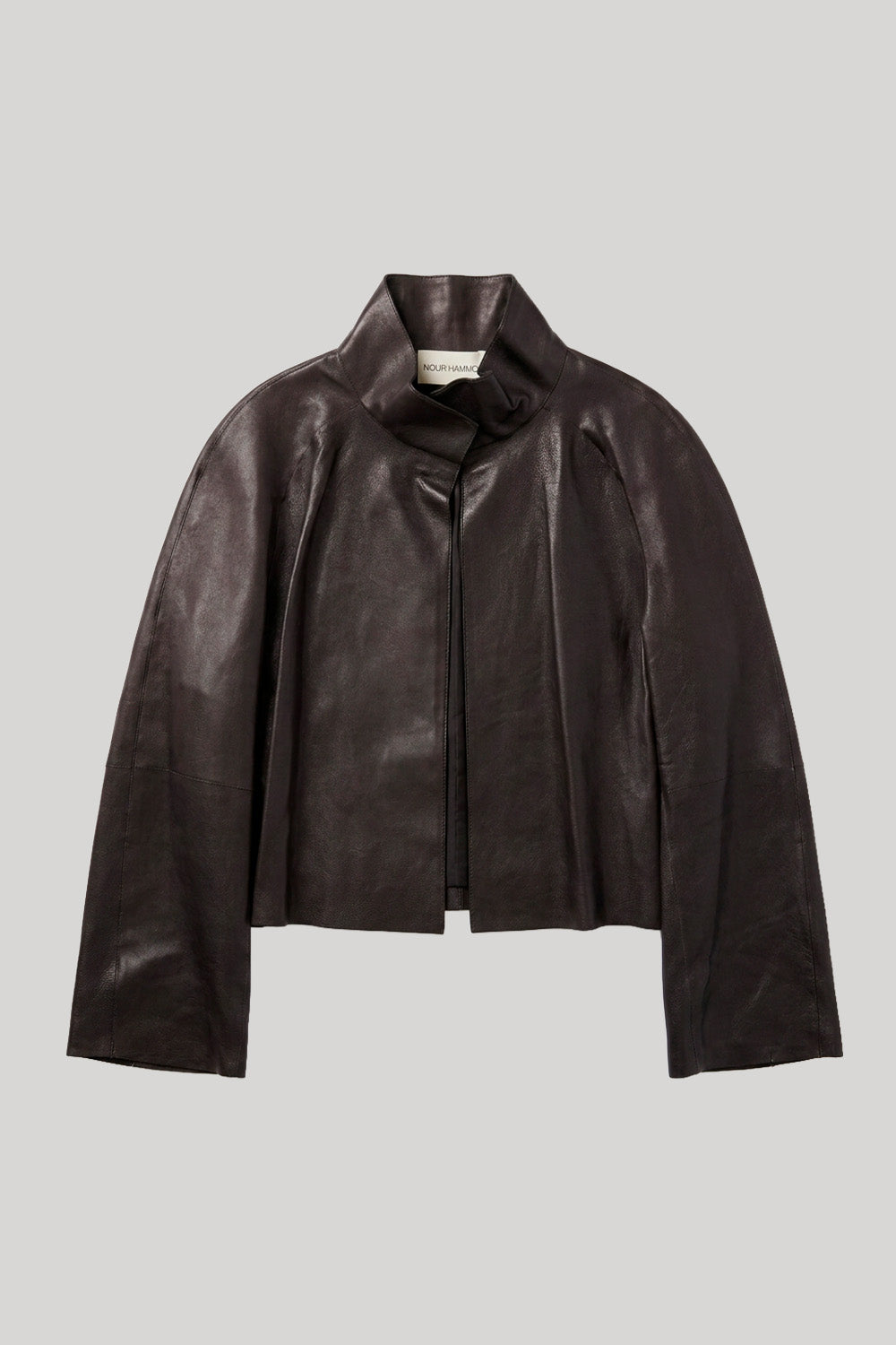 A dark brown cropped leather jacket with a high structured collar and long sleeves, displayed flat against a solid light gray background. The jacket is from Nour Hammour.