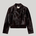 A dark brown cropped pony hair leathre jacket with a pointed collar and three-quarter sleeves, shown flat on a light gray background. The jacket is from Nour Hammour