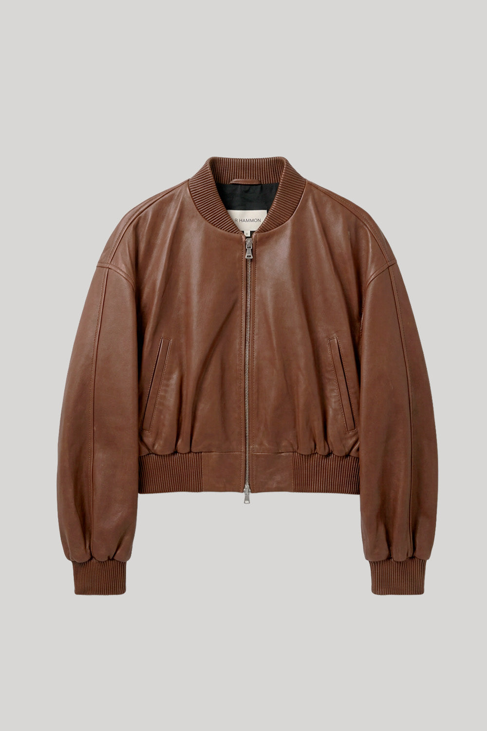 A brown leather bomber jacket with a ribbed collar, cuffs, and hem, featuring a front zipper and side pockets, shown against a solid light gray background. The jacket is from Nour Hammour