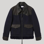 A dark navy blue shearling-style jacket from Parosh with black leather shoulder panels, collar, and cuffs, featuring a front zipper and two flap pockets, shown against a solid gray background.