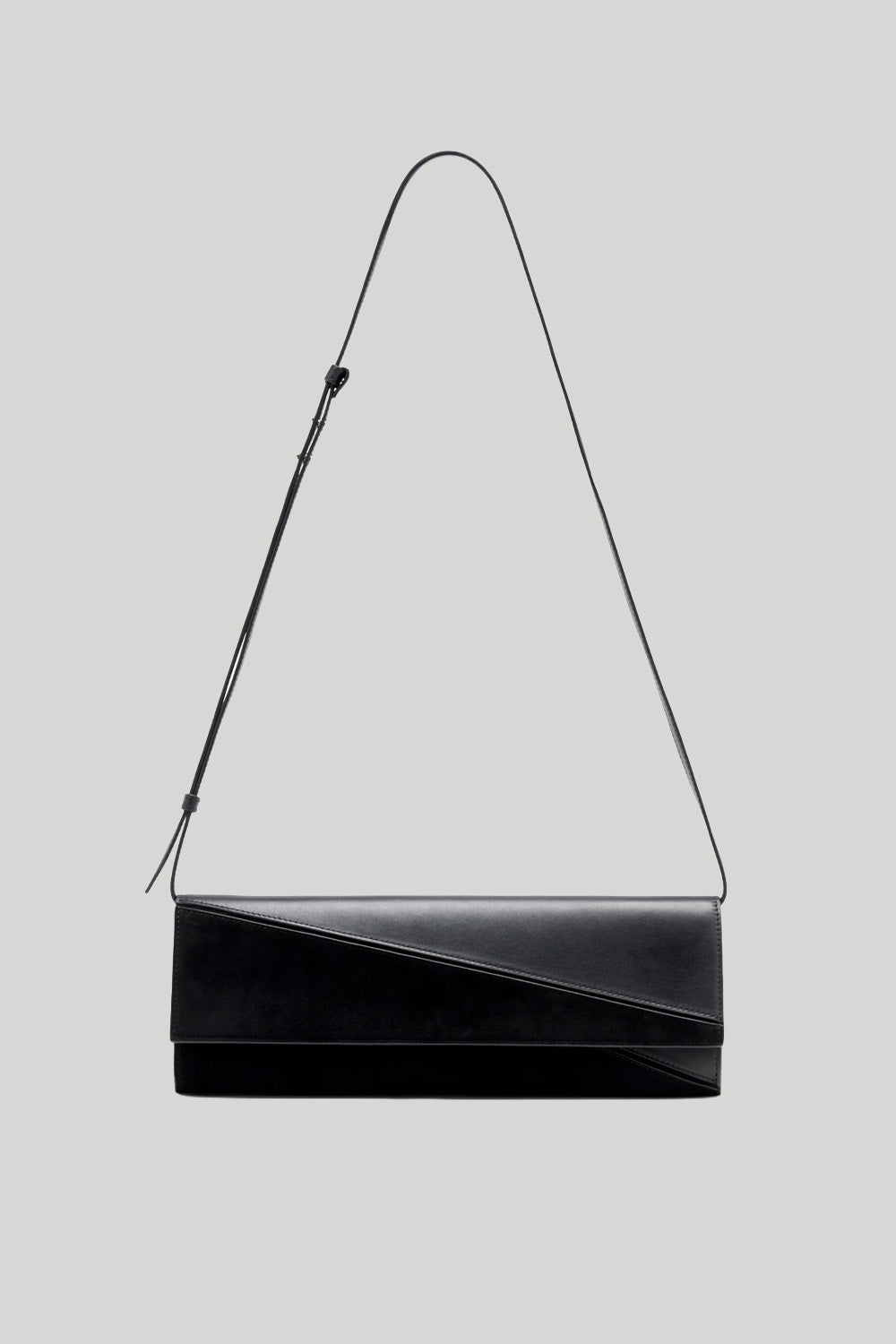 A black leather shoulder bag with an asymmetrical diagonal flap and a thin black strap, shown against a solid light gray background.