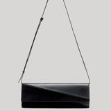 A black leather shoulder bag with an asymmetrical diagonal flap and a thin black strap, shown against a solid light gray background.