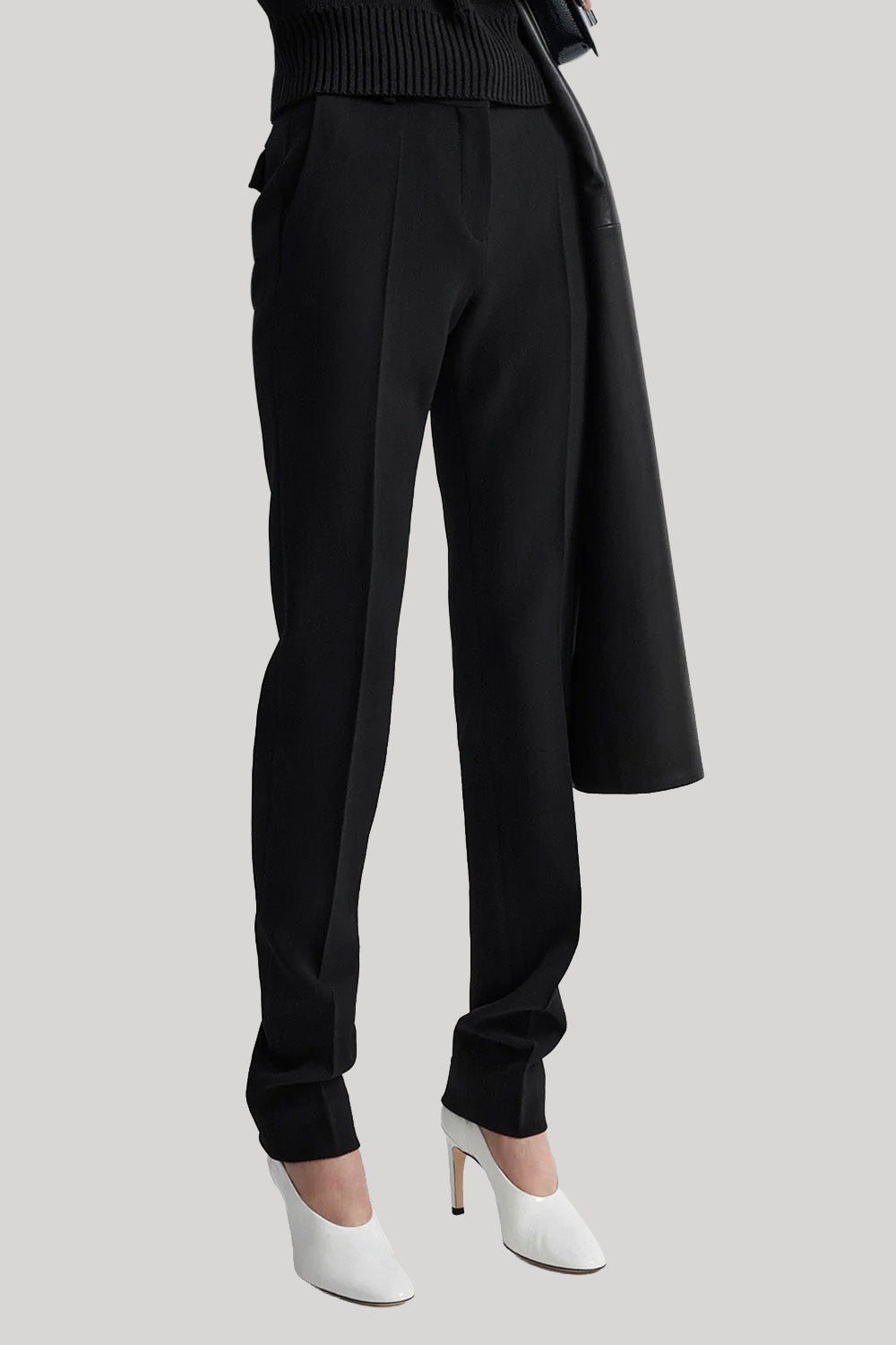Black wide-leg trousers with a draped coat and white pointed-toe heels, shown on a model from the waist down against a light gray background.