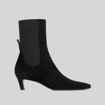 A black suede ankle boot with a square toe and a slim black kitten heel, featuring a black elastic side panel, shown against a solid light gray background.