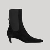 A black suede ankle boot with a square toe and a slim black kitten heel, featuring a black elastic side panel, shown against a solid light gray background.