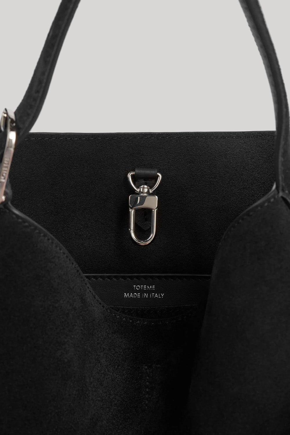 Close-up of the interior of a black tote bag with a silver metal D-ring clasp and a small white 'TOTEME MADE IN ITALY' label stitched inside.