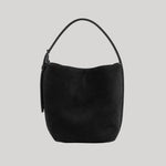 A black suede crescent-shaped Toteme shoulder bag with a single top handle, shown against a solid light gray background. 