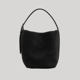 A black suede crescent-shaped Toteme shoulder bag with a single top handle, shown against a solid light gray background. 