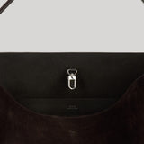 Close-up of a dark brown suede shoulder bag from Toteme with a silver metal D-ring clasp on a light gray background.