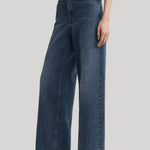 A model wearing a pair of high-waisted, wide-leg blue denim jeans from Toteme, styled with a white top and black pointed-toe heels against a light gray studio background.