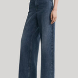 A model wearing a pair of high-waisted, wide-leg blue denim jeans from Toteme, styled with a white top and black pointed-toe heels against a light gray studio background.