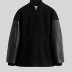 A black button-front jacket with contrasting black leather sleeves, shown against a solid light gray background. 