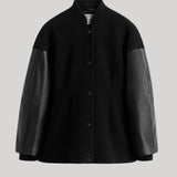 A black button-front jacket with contrasting black leather sleeves, shown against a solid light gray background. 